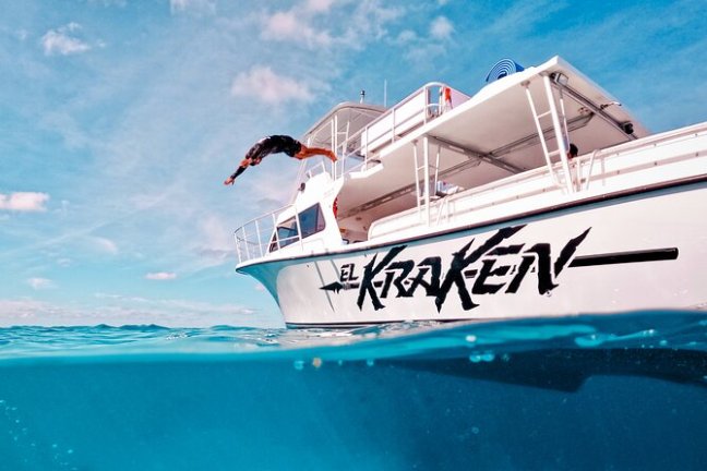 Person dives off a boat named 'El Kraken' into clear ocean water.