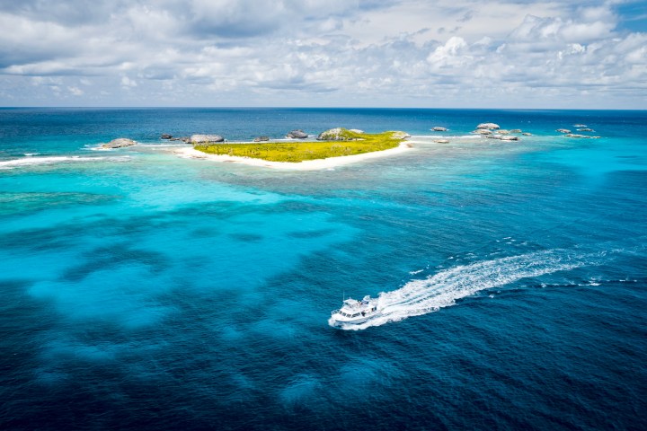 Boat sailing near a small island with blue waters and cloudy sky.