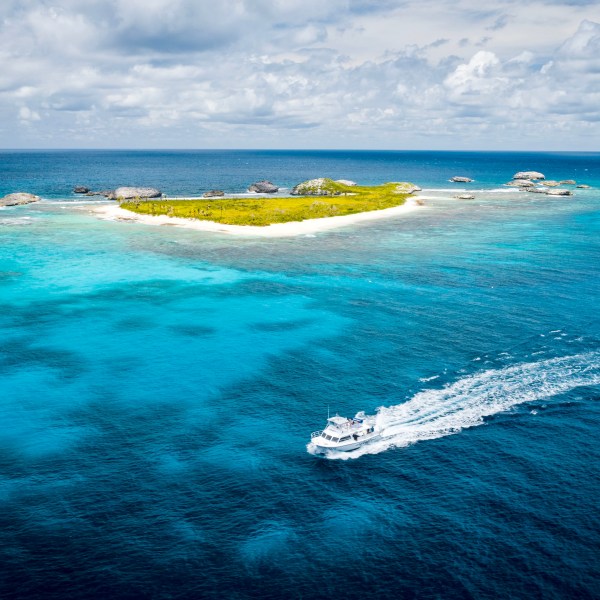 Boat sailing near a small tropical island with clear blue water and cloudy sky.