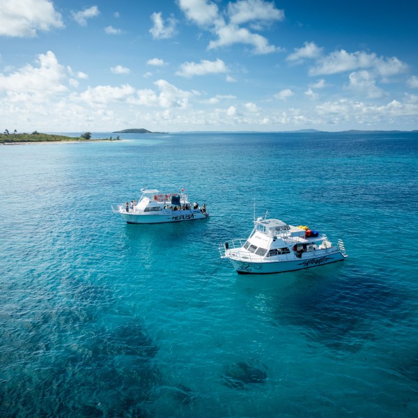 Two boats on clear blue ocean, distant coastline and sky with clouds.