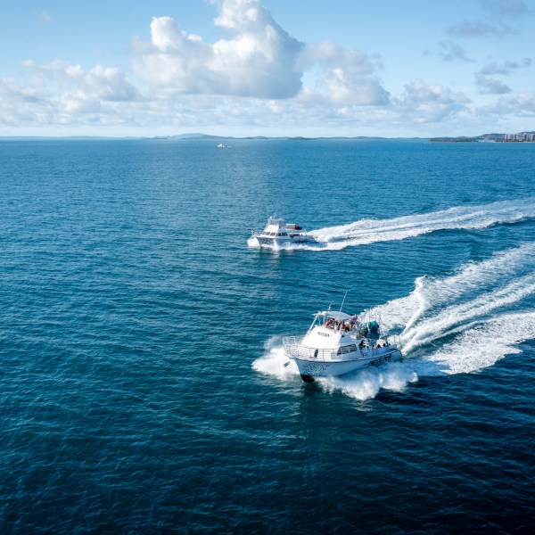 Two boats speed across a calm blue ocean under a partly cloudy sky.