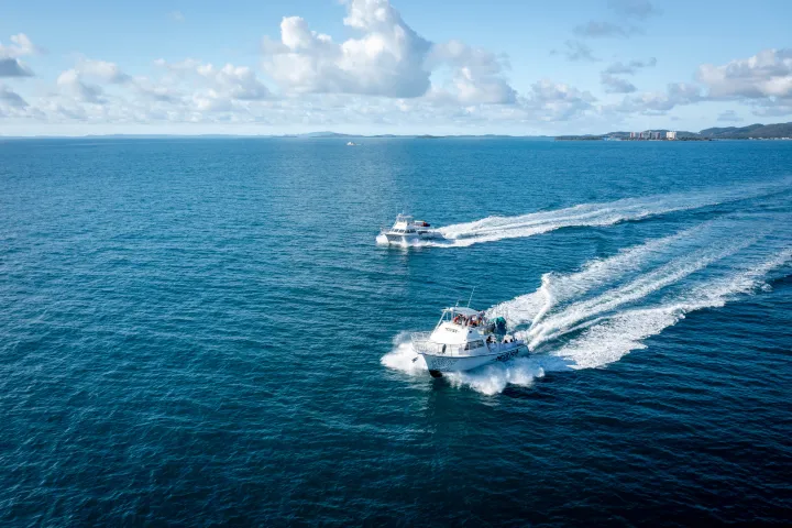 Two boats speed across a calm blue ocean under a partly cloudy sky.