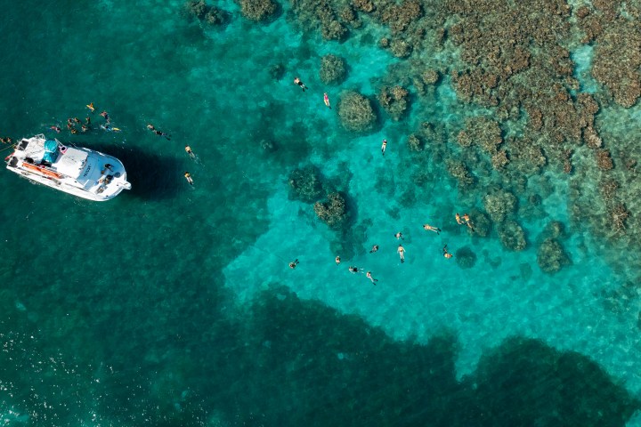 Aerial view of a boat near snorkelers in clear blue water above coral reefs.