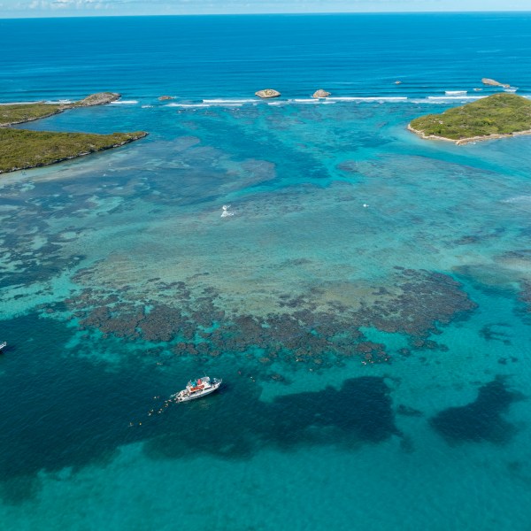 Aerial view of turquoise sea with coral reefs and boats near small islands.