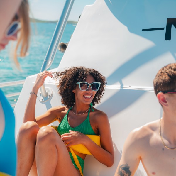 Three people in swimsuits on a boat, smiling and wearing sunglasses.