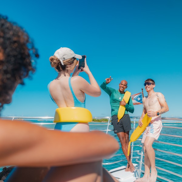 People on a boat posing for a photo with life vests under a clear blue sky.