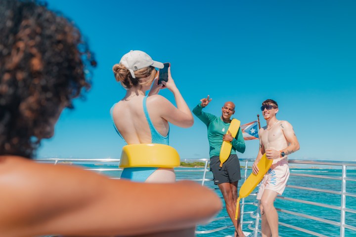 People on a boat posing for a photo with life vests under a clear blue sky.