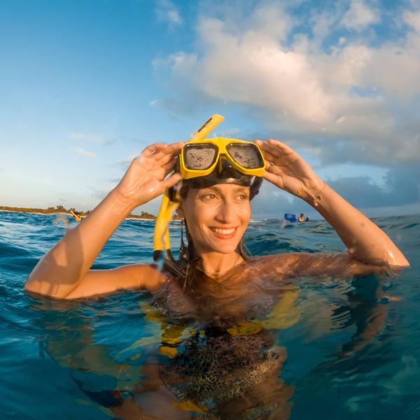 Woman in water wearing a snorkel mask at sunset.