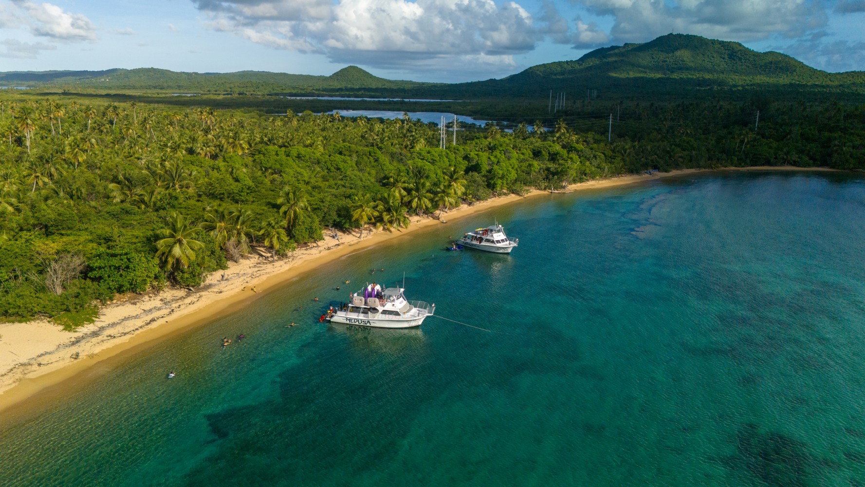 Aerial view of a beach with palm trees, two boats, and turquoise water.