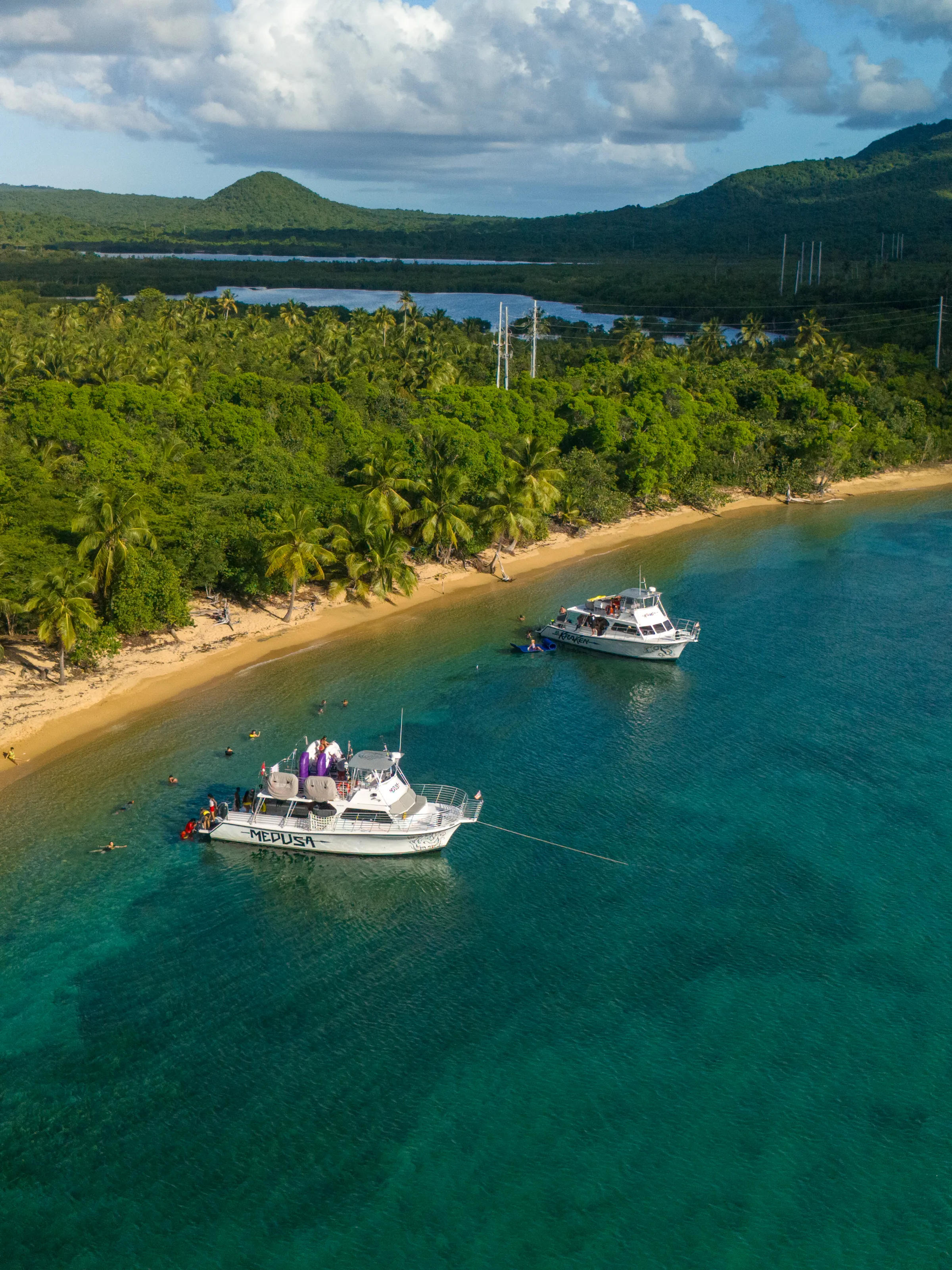 Aerial view of a beach with palm trees, two boats, and turquoise water.