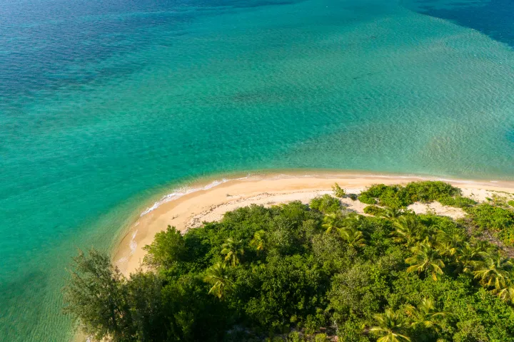 Aerial view of a lush green island with a sandy beach surrounded by turquoise ocean.