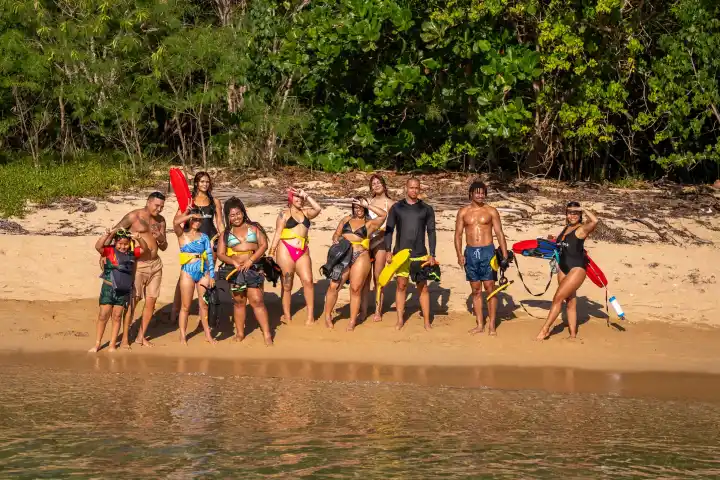 Group of people in swimwear holding snorkeling gear on a beach.