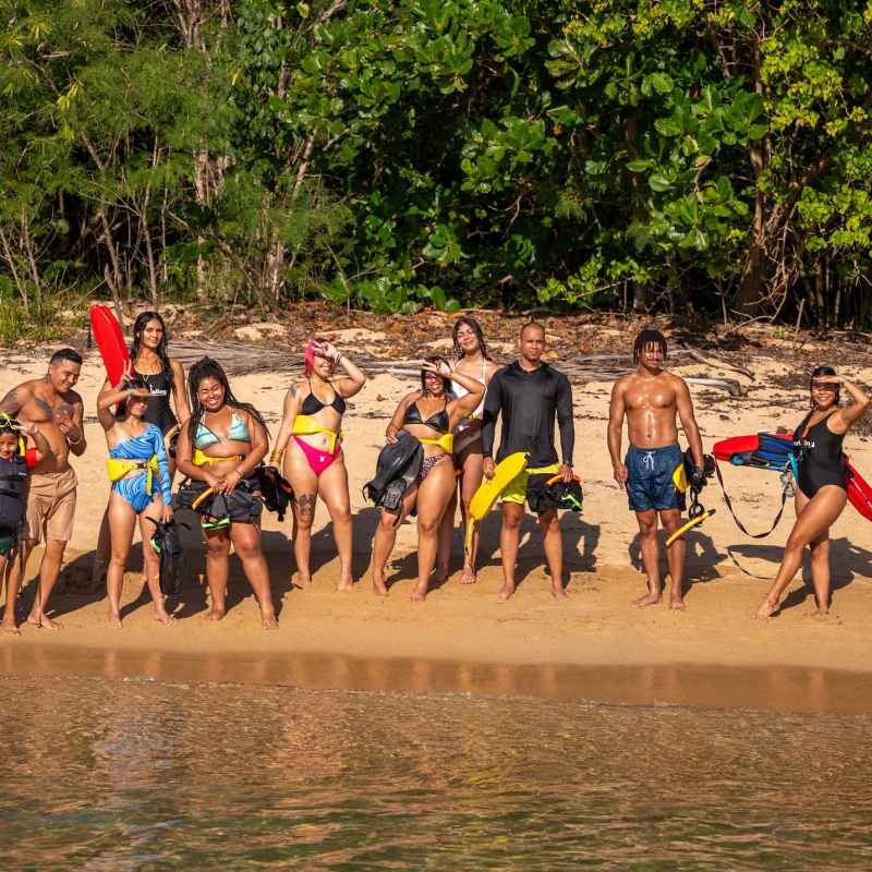 Group of people in swimwear holding snorkeling gear on a beach.