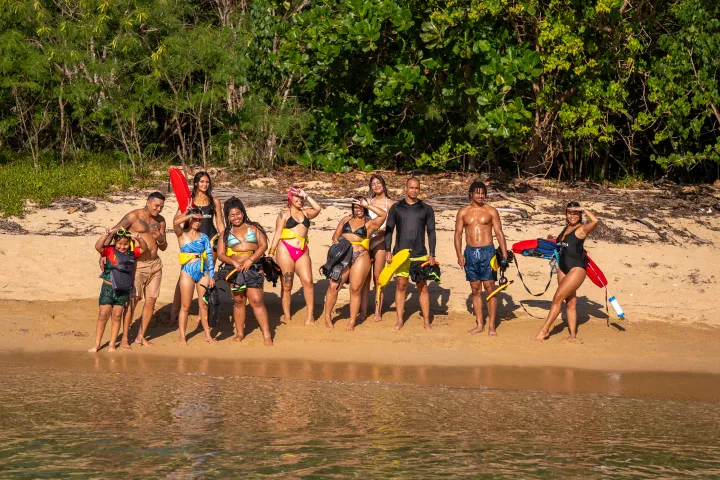 Group of people in swimsuits standing on a sandy beach with snorkeling gear.