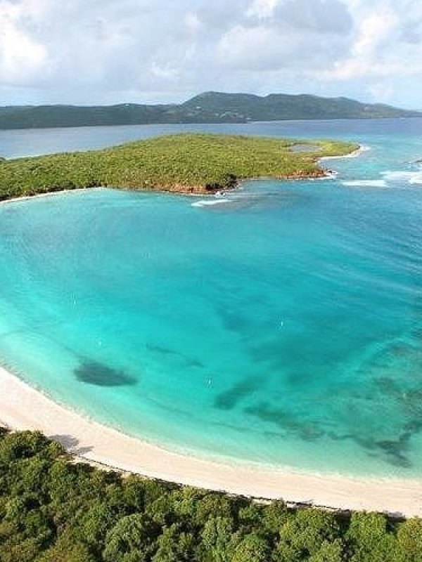 Aerial view of a curved tropical beach with turquoise waters and lush greenery.